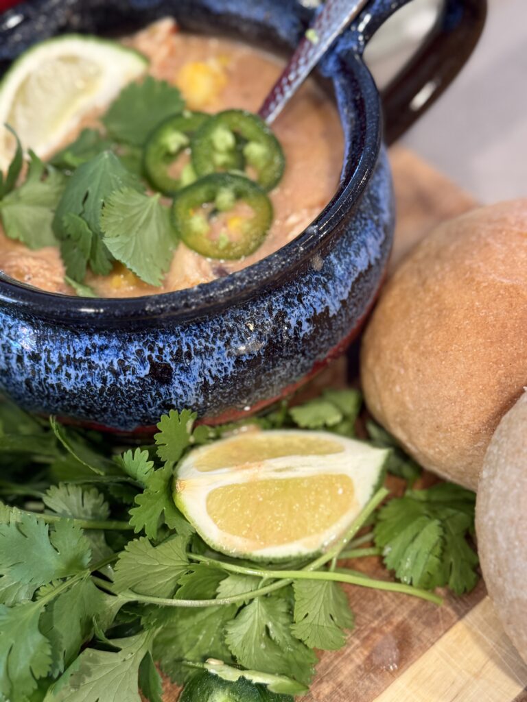 Creamy roasted poblano chicken tortilla soup topped with fresh cilantro and sliced jalapenos with fresh milled flour bread on the side